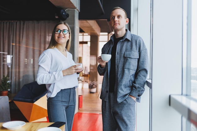 A businessman and a business woman are drinking coffee together standing in front of the windows of an office building overlooking the city Two confident businessmen working in a modern office