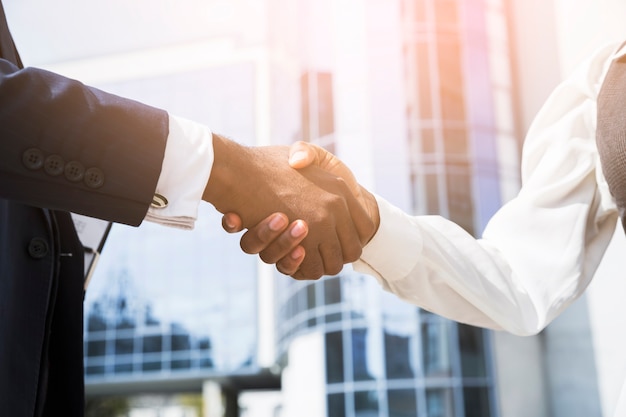 Businessman and businesswoman shaking hands in front of corporate building