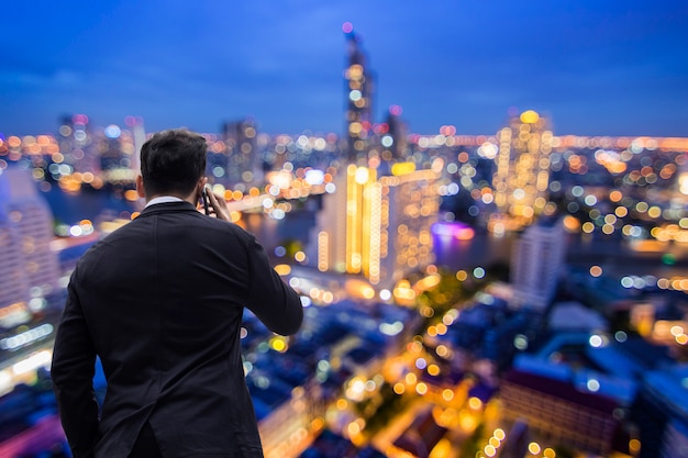 Businessman calling phone on top of tower with night city background