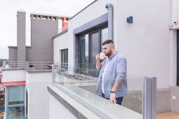 Businessman in casual clothes relaxing on the terrace overlooking the city uses the phone and uses a laptop while drinking coffee