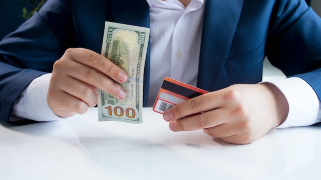 Businessman choosing between paper money banknotes and plastic redit card.