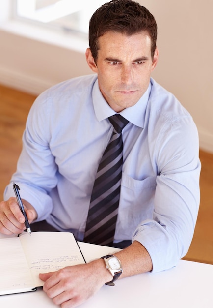 Businessman at desk thinking writing and notes for market research business plan and insight at startup Office notebook and man with schedule agenda or to do list in book with ideas for project