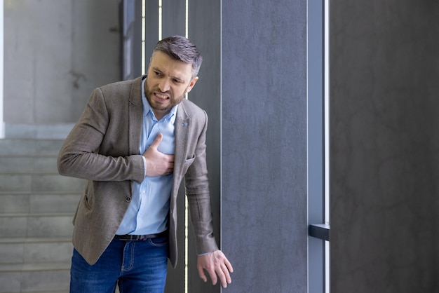 Businessman in distress clutching chest by office door depicting heart attack health crisis or