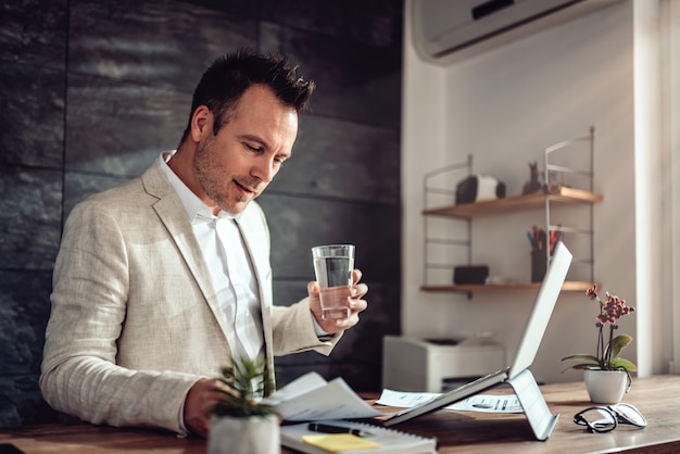 Businessman doing paperwork in his office and holding glass of water