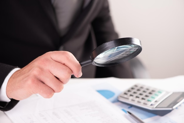 Businessman examining document with magnifying glass