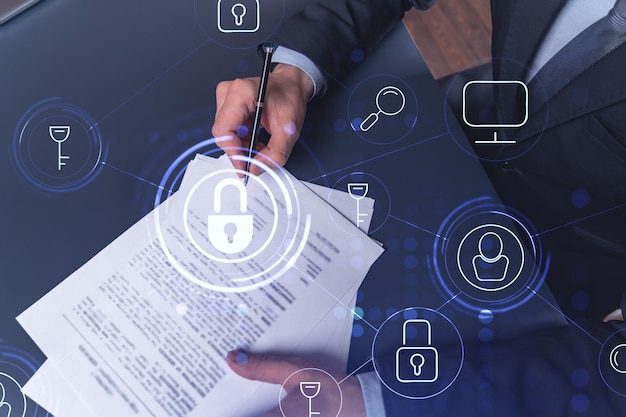 A businessman in formal wear signing the contract to prevent probability of risks in cyber security Padlock Hologram icons over the working desk