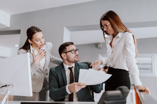 Businessman in formal wear talking with his female colleagues about documents while sitting in modern office.