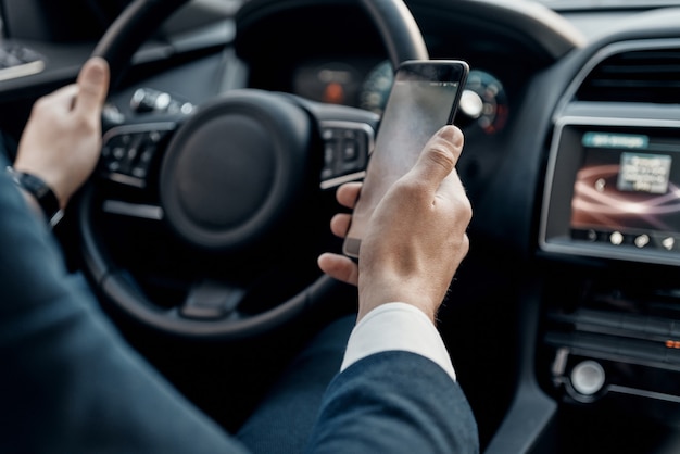 Businessman on the go. Close up top view of young man in formalwear holding a smart phone while driving a luxury car