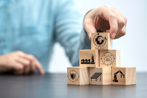 Businessman hand arranging wood block with net zero icon Net zero by 2050 Carbon neutral energy or Net Zero greenhouse gas emission target on wooden cubes background