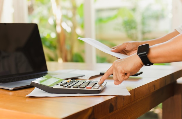 Businessman hand on calculator to calculate financial report and laptop computer on table