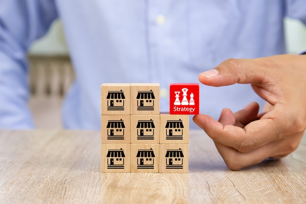 Businessman hand choose red color wooden block with business strategy icon.