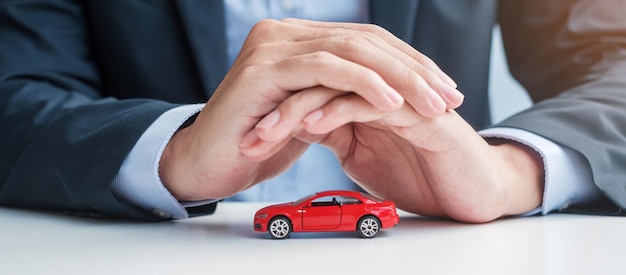 Businessman hand cover or protection red car toy on table Car insurance warranty repair Financial banking and money concept