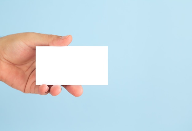 Businessman hand holding blank business card on light blue background.