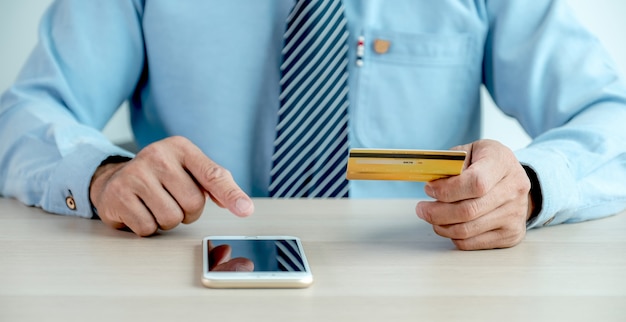 Businessman hand  holding credit card and use smartphone to online shopping from home, payment e-commerce, internet banking, spending money for next holidays.