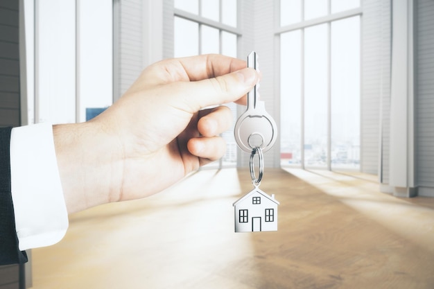 Businessman hand holding key with house chain in interior with city view and sunlight Rent concept 3D Rendering