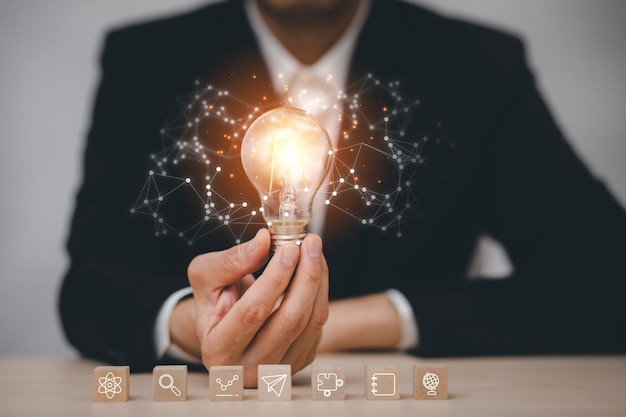 Businessman hand holding light bulb with icon on wood cube and   working on desk Creativity and innovation are keys to successConcept of new idea and innovation with Brain and light bulbs working a