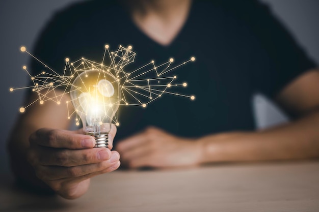 Businessman hand holding light bulb with icons and working on the desk Creativity and innovation are keys to successConcept of new idea and innovation with energy and power working at home