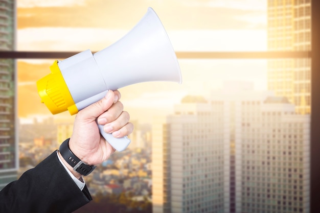 Businessman hand holding megaphone with office building background