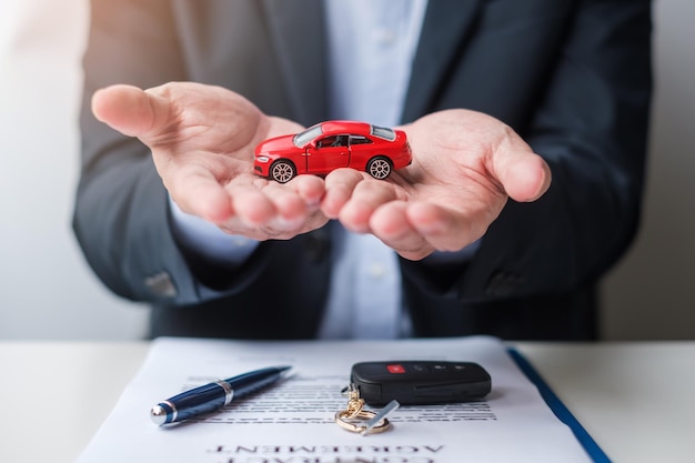 Businessman hand holding red car toy with vehicle keyless pen and contract document buy and sale insurance rental and contract agreement concepts