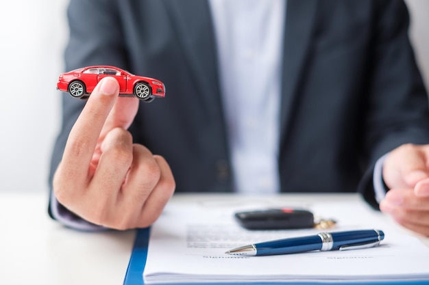 Businessman hand holding red car toy with vehicle keyless pen and contract document buy and sale insurance rental and contract agreement concepts