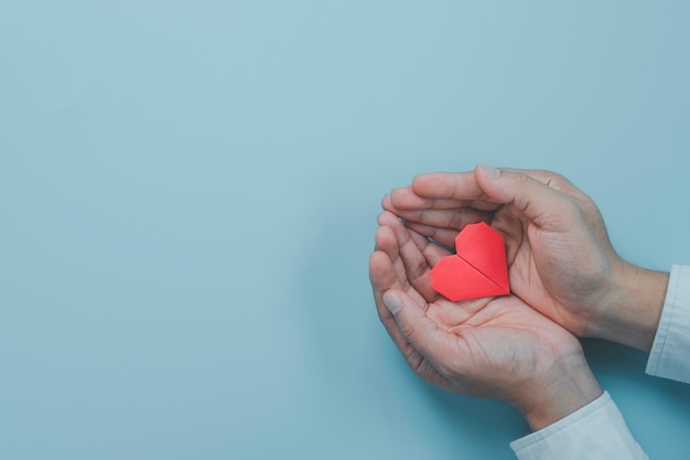 Businessman hand holding red heart paper with heart wave signal on blue background. It is health check condition concept.