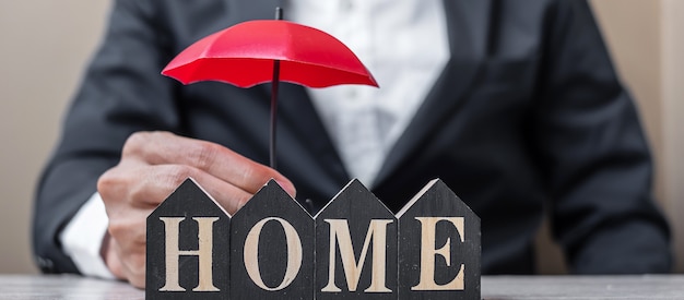 Businessman hand holding red Umbrella cover wooden Home model on table office.