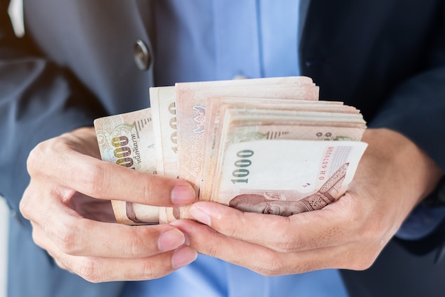 Businessman hand holding Thai Baht banknote stack.