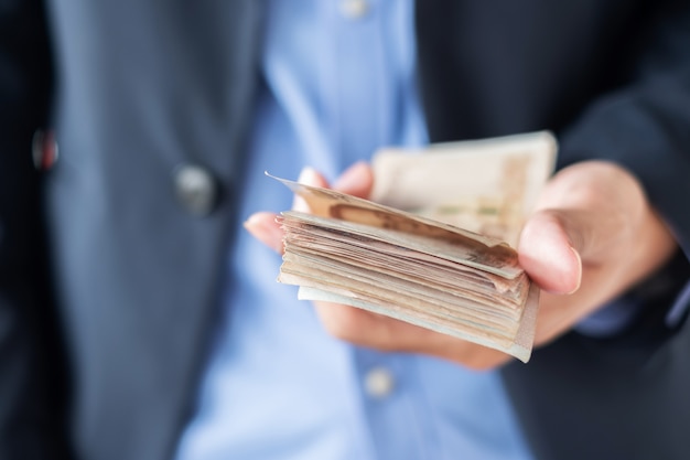 Businessman hand holding Thai Baht banknote stack.