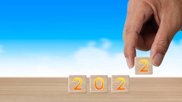 Businessman hand holding wooden cube block with number 2022 on table, new year calendar concept