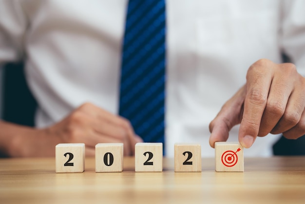 Businessman hand holding woods cube with new year icon word 2022 and goal target icon