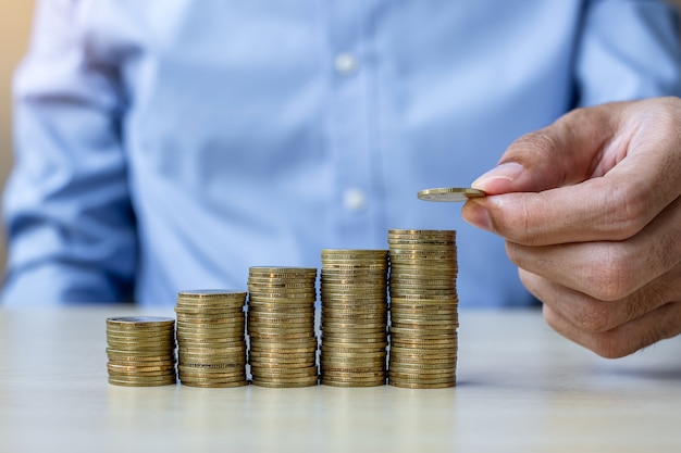 Businessman hand putting golden coin on growing money stairs 