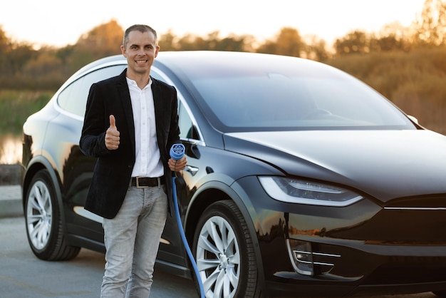 Businessman hand showing thumbs up holding power type ccs cable supply plugged at electric car