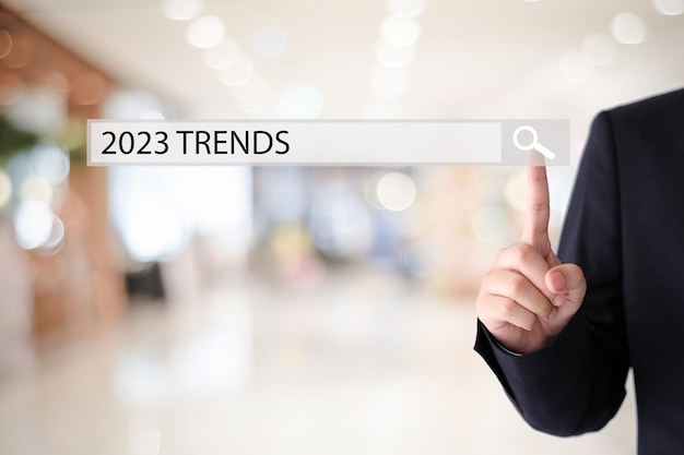 Businessman hand touching 2023 trends search bar over blur office background