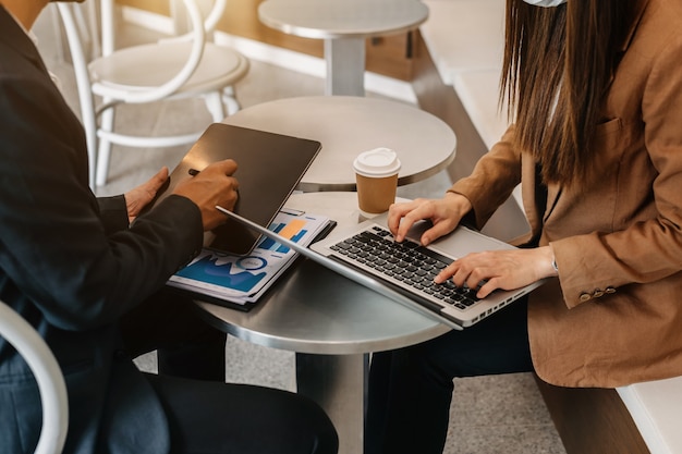 Businessman hand using smartphone, laptop and tablet with social network diagram and two colleagues discussing data on desk as concept in morning light.