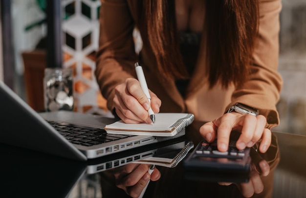 Businessman hand working at a computer and writing on a notepad with a pen in the office on the desk there a calculator