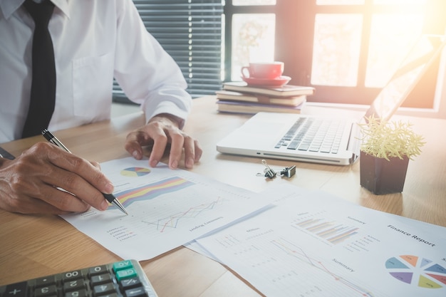 Businessman hand working with financial data and calculator on white desk in modern office