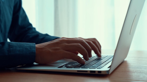 Businessman hand works on capable laptop computer at office table close up shot