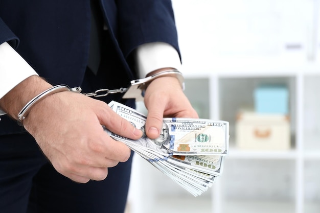 Businessman in handcuffs holding bribe indoors closeup