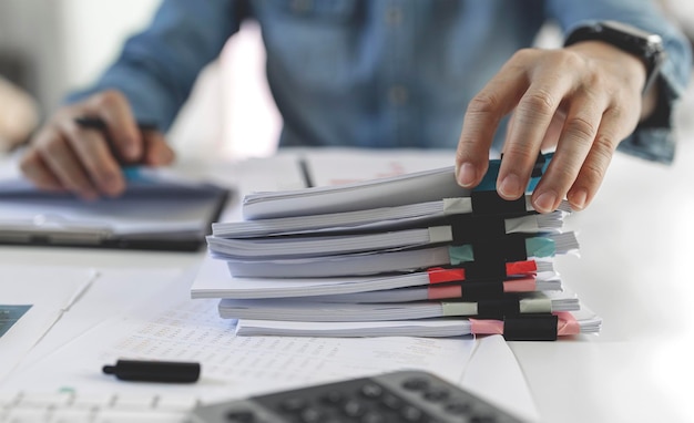 Businessman hands working in Stacks of paper files for searching and checking unfinished document achieves on folders papers