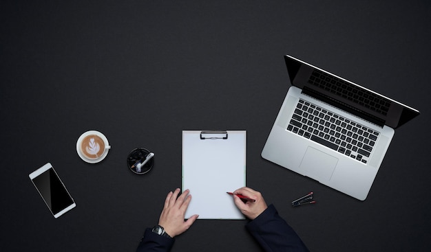 Businessman hands writing on white paper with office supplies . Flat lay and top view with copy space on black background .business desk  lifestyle concept.