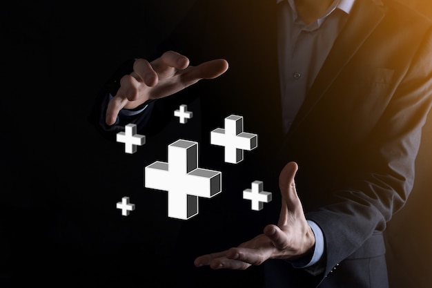 Businessman hold 3D plus icon, man hold in hand offer positive thing such as profit, benefits, development, CSR represented by plus sign.The hand shows the plus sign.