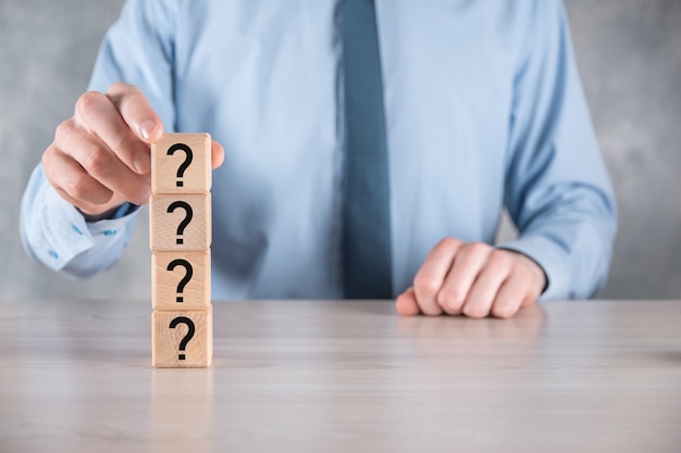 Businessman hold and put wooden cube block shape with question marks on grey table. Space for text.concept for confusion, question or solution.