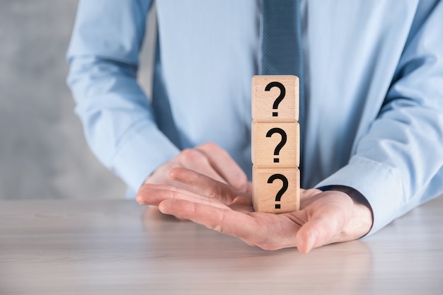 Businessman hold and put wooden cube block shape with question marks on grey table