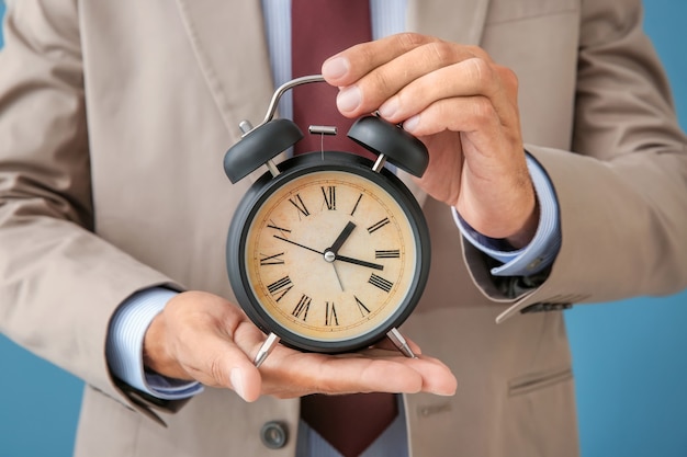 Businessman holding alarm clock, closeup. Time management concept