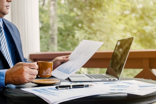 Businessman holding coffee cup analysis the graph with laptop at the home office