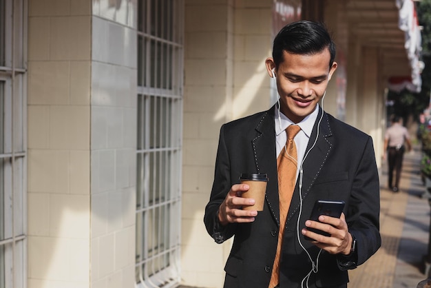 Businessman holding a coffee and listening to music through earphones while walking through the city