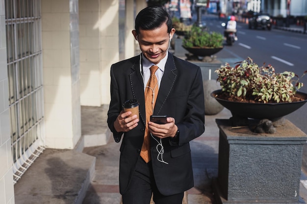 Businessman holding a coffee and listening to music through earphones while walking through the city