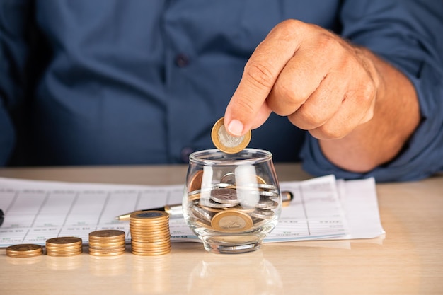 Businessman holding coins and putting into glass pot. Saving concept for financial accounting.