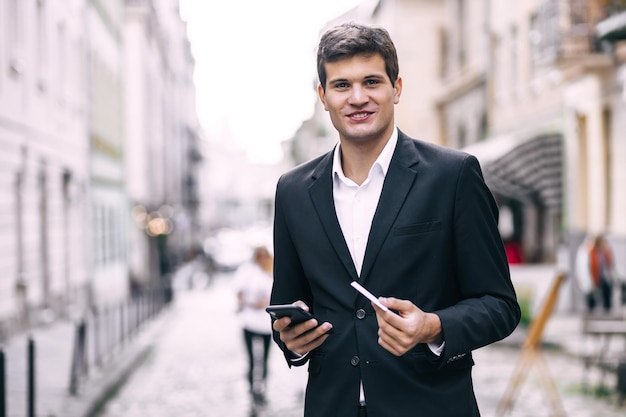 Businessman holding a credit card and making online payments on his mobile phone happy man standing on city street