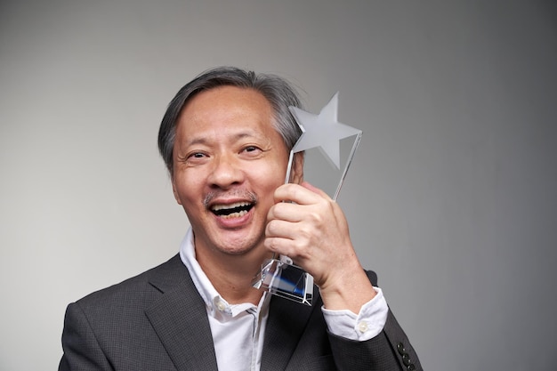 Businessman holding crystal star trophy against gray background